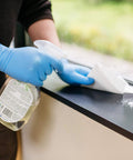 Person wearing Textured Blue Nitrile Gloves 5 Mil Powder Free Food Safe Large Box Of 100 while cleaning a surface with spray bottle
