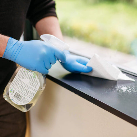 Person wearing Textured Blue Nitrile Gloves 5 Mil Powder Free Food Safe Large Box Of 100 while cleaning a surface with spray bottle