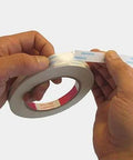 Hands holding and peeling Three Eighths Inch Double Sided Adhesive Tape, 27 Yards Per Roll, Two Roll Pack, Acid Free Ultra Thin White Tape.