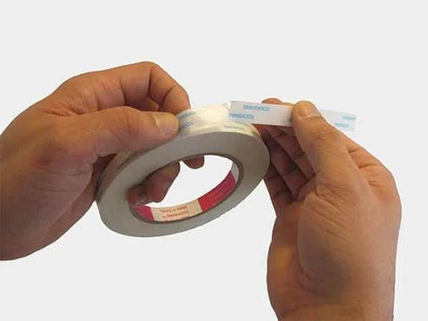Hands holding and peeling Three Eighths Inch Double Sided Adhesive Tape, 27 Yards Per Roll, Two Roll Pack, Acid Free Ultra Thin White Tape.