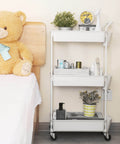 Three Tier Utility Rolling Cart With Lockable Caster Wheels And Three Hanging Baskets beside a bed with teddy bear.