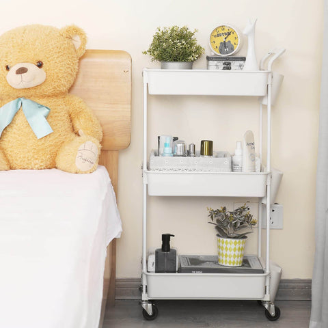 Three Tier Utility Rolling Cart With Lockable Caster Wheels And Three Hanging Baskets beside a bed with teddy bear.