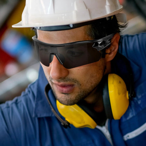 Worker wearing 3 Pack Tinted Safety Glasses ANSI Z87.1 Protective Eyewear For Work And Shooting, hard hat, and ear protection