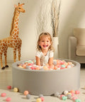 Child playing in gray ball pit with colorful star and heart shaped ball pit balls, giraffe decor in background. Ball Pit Balls,Plastics Balls for Ball Pit, Stars Hearts Shape for PastelBall for Toddlers Kids，6 Mix Colors,50pcs