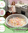 Toddler with gray ball pit filled with plastic balls in pink, gold, pearl white, and clear colors in a kitchen setting.