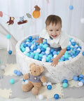 Child playing in a marble-patterned ball pit filled with blue and white plastic play balls, surrounded by toys, featuring Ball Pit Balls for Kids.