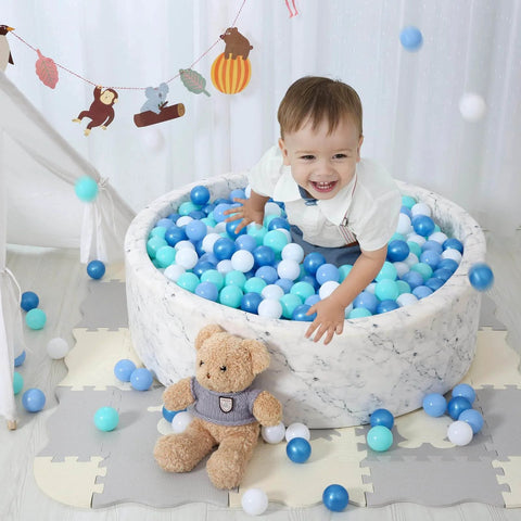 Child playing in a marble-patterned ball pit filled with blue and white plastic play balls, surrounded by toys, featuring Ball Pit Balls for Kids.