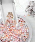 Child sliding into ball pit filled with 100-pack hollow plastic balls in pink, gold, pearl white, clear; safe playtime for toddlers.