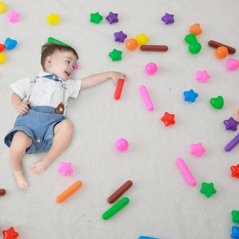 Toddler playing with ball pit balls surrounded by colorful shapes on a white surface