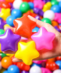 Hand holding star-shaped ball pit balls in rainbow colors. Ball Pit Balls for Toddlers - 50 Count Star Balls Different Shapes for Festival Indoor Outdoor, Party Decoration for Babies Kids (Rainbow). Non-toxic play balls.