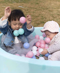 Toddlers playing with pink and blue toy balls in a light blue ball pit outdoors