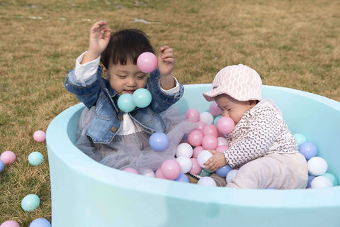 Toddlers playing with pink and blue toy balls in a light blue ball pit outdoors