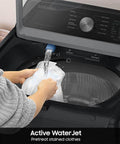 Smart Laundry Bundle With 4.7 Cu Ft Top Load Washer And 7.4 Cu Ft Electric Dryer WaterJet System Sensor Drying Prevents Overdrying Low Vibration Quiet Wash Includes Power Cords Hoses Vent Duct And 1 Year CPS Protection Black showing active WaterJet with hands placing clothes in washer.