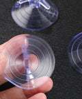 Hand holding a 45mm transparent PVC aquarium suction cup from the 12 pack for glass surfaces, showing vacuum ring design for secure mounts.