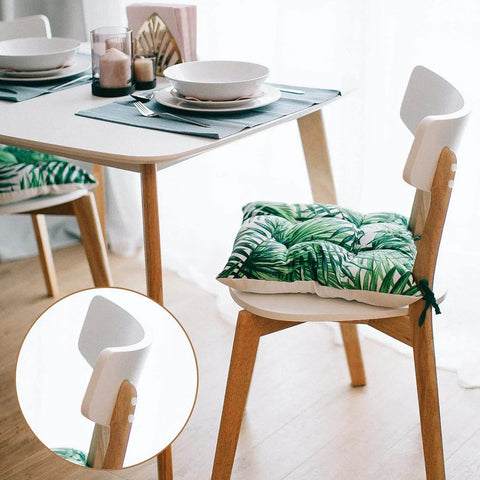 Dining chair with green leaf-patterned cushion at a set table with plates and candles.
