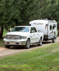 White pickup truck towing a Geo Pro RV trailer on a forest path.