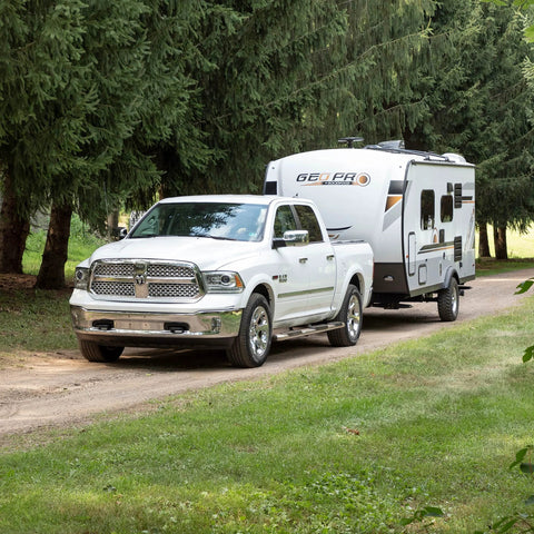 White pickup truck towing a Geo Pro RV trailer on a forest path.