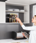 Woman using Two Tier Rotating Spice Organizer Turntable in kitchen cabinet, adjustable shelves fit tall bottles, olive oil, seasonings.