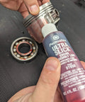 Permatex 81950 Ultra Slick Engine Assembly Lube, 4 oz., Red bottle next to metal engine bearings on a workbench.