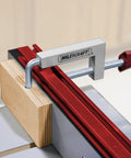 Milescraft 7209 universal fence clamp, silver aluminum body with red knob, clamping wood to a red fence.