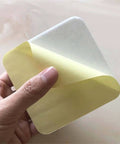 Hand holding a corner of a 4-Piece Vacuum Tech Rug Pad Gripper for Hardwood Floors and Under Rugs Tape, showing adhesive side.