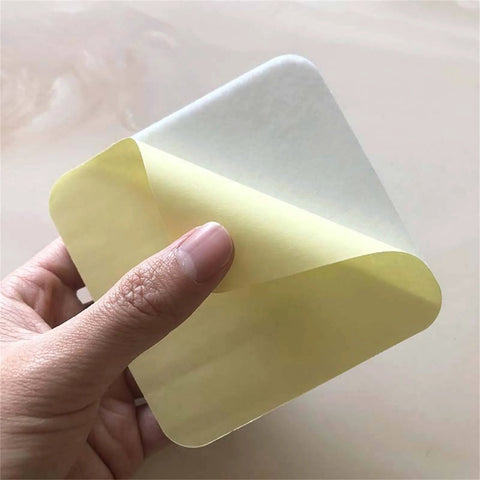 Hand holding a corner of a 4-Piece Vacuum Tech Rug Pad Gripper for Hardwood Floors and Under Rugs Tape, showing adhesive side.