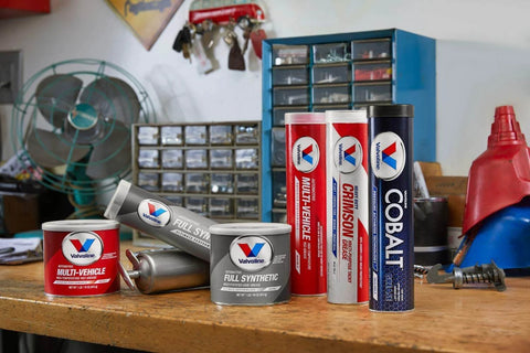Valvoline multi-vehicle and full synthetic grease products on a workbench in an automotive workshop setting.