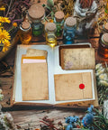 Open scrapbook with Pro Grade File Pocket Metal Die Cuts Set for card making and scrapbooking, surrounded by colorful bottles and flowers.