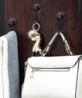 Coat and bag hanging on black hooks attached to a dark wooden surface, with a dinosaur keychain on the bag.