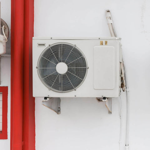 Outdoor air conditioning unit mounted on a white wall with red accents.