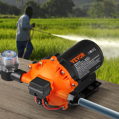 Water Diaphragm Pump, 12V DC, 5.5 GPM Flow, 70 PSI Rated Pressure (40-100 PSI Adjustable), 1/2" MNPT Self Priming Sprayer Pump with Pressure Switch for RV Camper Marine Boat Lawn, FCC Certified shown on a wooden surface with a field in the background.