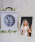 Decorative white clock with flowers beside framed bridal portrait on stand