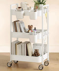 Versatile 3 Tier Rolling Cart With Locking Wheels Hanging Cups And Hooks Heavy Duty Metal Storage Organizer For Kitchen Office Bathroom Craft Room White Perfect For Spices Toiletries Craft Supplies Makeup And More shown loaded with books, plants, and utensils on wooden floor