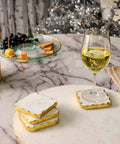 16 inch white marble lazy susan with gold edge displaying snacks and a glass of white wine on a marble table.