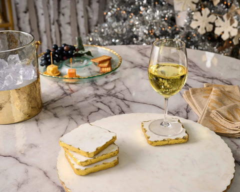 16 inch white marble lazy susan with gold edge displaying snacks and a glass of white wine on a marble table.