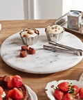 12 inch white marble lazy susan turntable with aluminum bearing holding snacks and desserts on a wooden table.