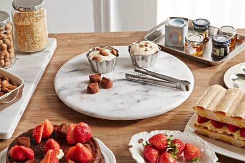 12 inch white marble lazy susan turntable with aluminum bearing holding snacks and desserts on a wooden table.