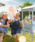 Outdoor party with children near a candy cart on wheels for parties with 40 balloons included, featuring desserts and decorations.