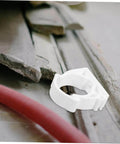 Single white clamp from 35 Piece Pipe Clamp Buckle Repair Kit For Water Pipes And Hoses placed near red hose and concrete debris.