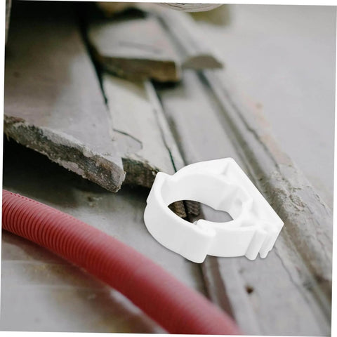 Single white clamp from 35 Piece Pipe Clamp Buckle Repair Kit For Water Pipes And Hoses placed near red hose and concrete debris.