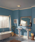 Round White Bath Exhaust Fan With Light And Glass Lens, 100 CFM installed in blue bathroom ceiling near mirror and sink area.