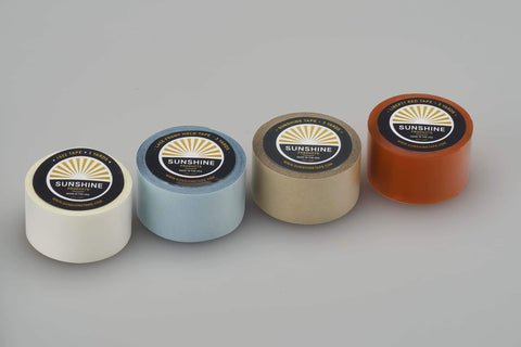 Four rolls of wig tape in different colors, including the Clear Double Sided Wig Tape For Daily Wear Stays Put Three Quarter Inch By Twelve Yards Premium Hair Adhesive Roll For Wigs Hair Systems Lace Bases Skin Bases Poly Perimeter On Lace Or Monofilament Bases Made In USA, arranged side by side on a gray background.