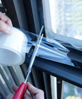 Applying Transparent Window Weather Sealing Tape 2 Inch x 33 FT with scissors for residue-free seal on windows.