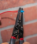 Kurve Wire Stripper Crimper Cutter Multi Tool for 10-26 AWG, cutting red wire against a brick wall, close-up of tool in use