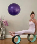 Woman exercising with yoga wheels and purple stability ball on display in a home gym setting.