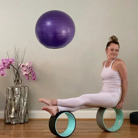 Woman exercising with yoga wheels and purple stability ball on display in a home gym setting.