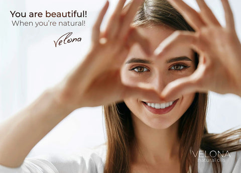 Smiling woman making heart shape with hands, Velona branding visible, promoting natural beauty, text reads 'You are beautiful when you're natural.'