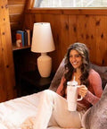 Stay hydrated on the go with this rugged 30 oz insulated stainless steel tumbler featuring FlowState three-position lid, a secure handle, and straw for easy sipping, BPA-free construction, cup holder friendly, in Rose Quartz 2.0 held by a person sitting on a bed.