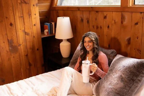 Stay hydrated on the go with this rugged 30 oz insulated stainless steel tumbler featuring FlowState three-position lid, a secure handle, and straw for easy sipping, BPA-free construction, cup holder friendly, in Rose Quartz 2.0 held by a person sitting on a bed.