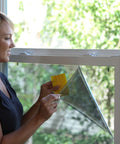 Woman using Complete Window Film Installation Kit For Residential Use with squeegee on window
